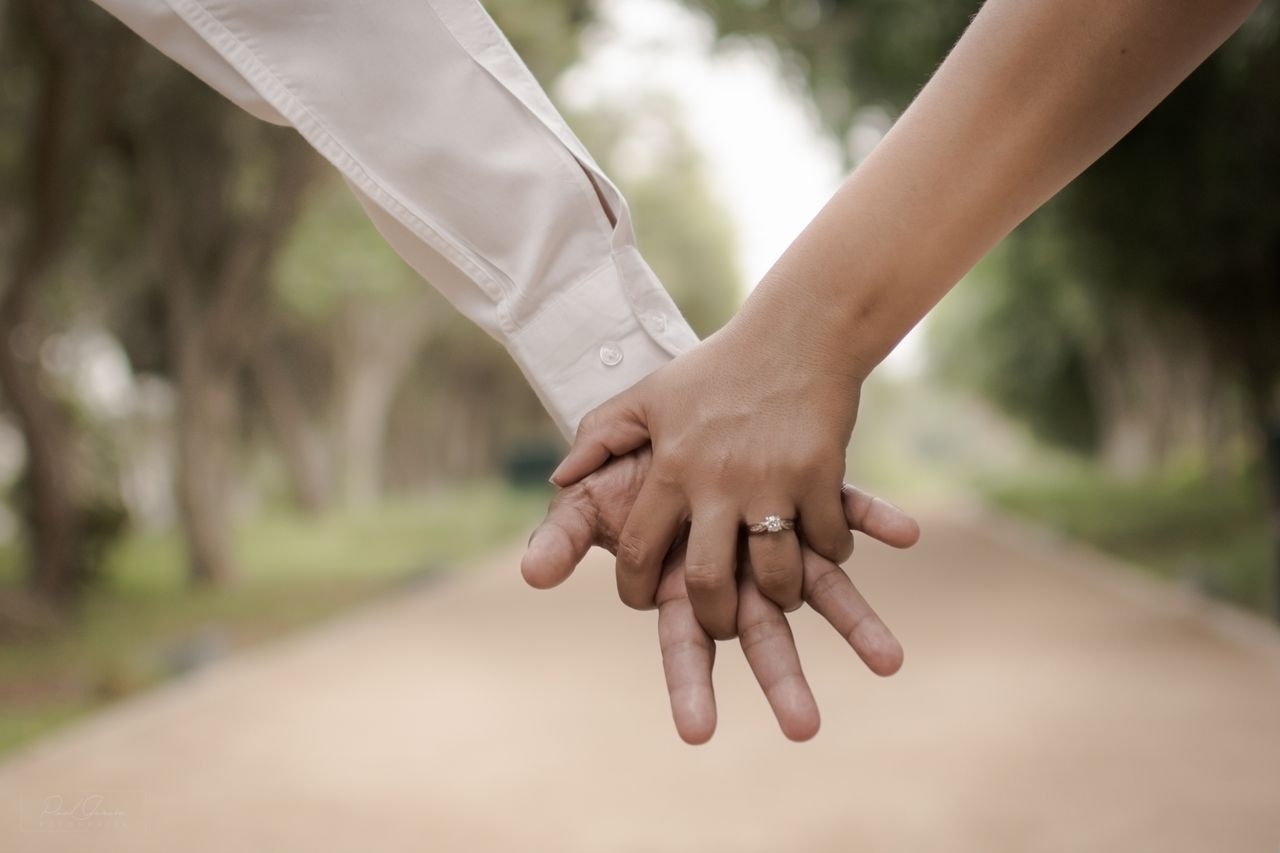 A couple holding hands shows off her engagement ring while walking down a street