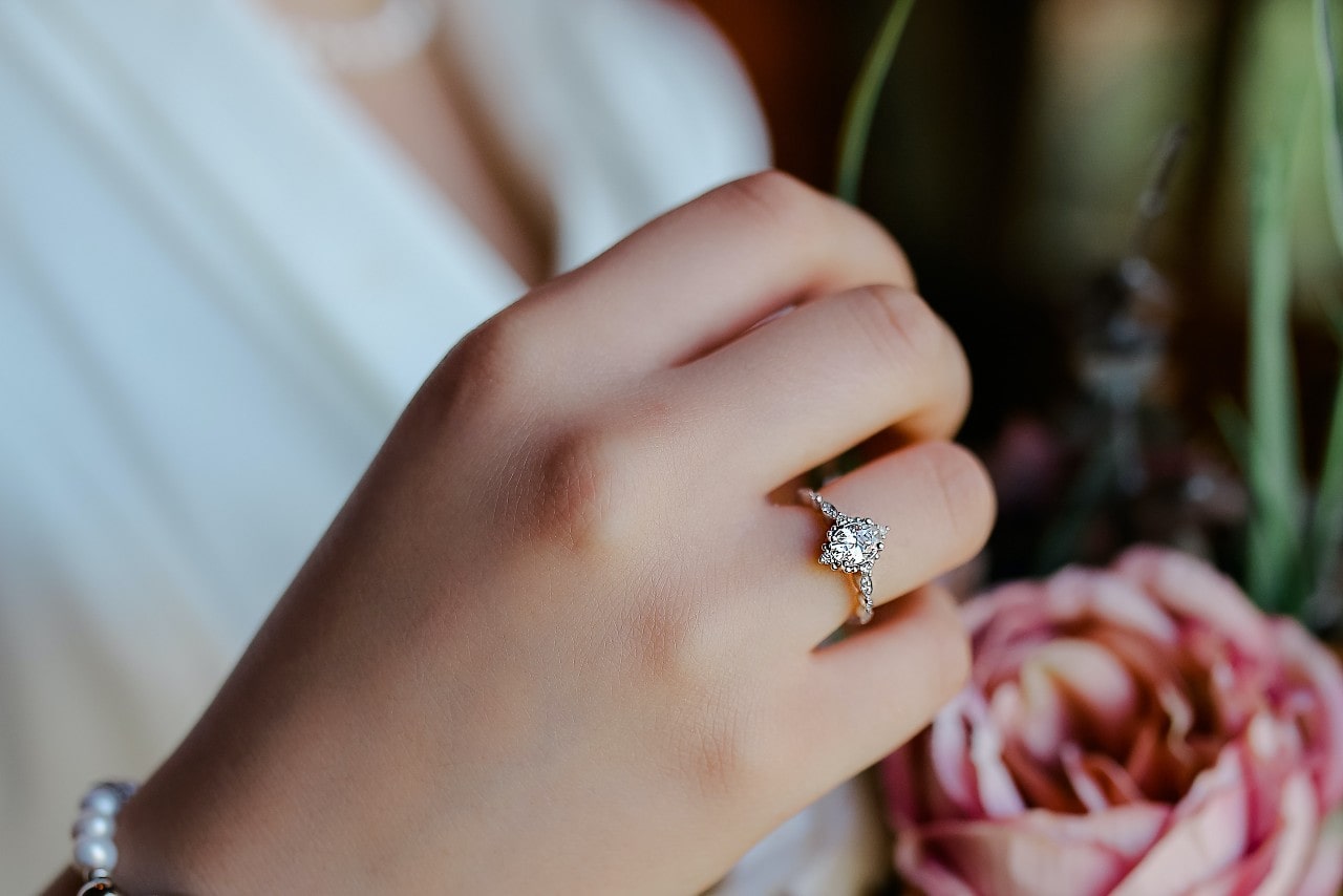 A woman wearing an engagement ring and a white shirt holds a flower