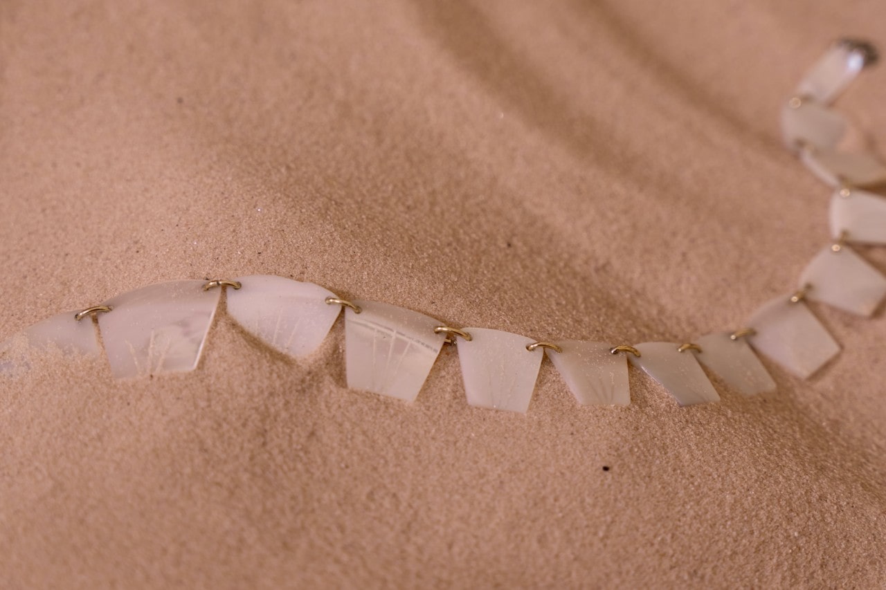 A seashell bracelet sits on the sand on the beach