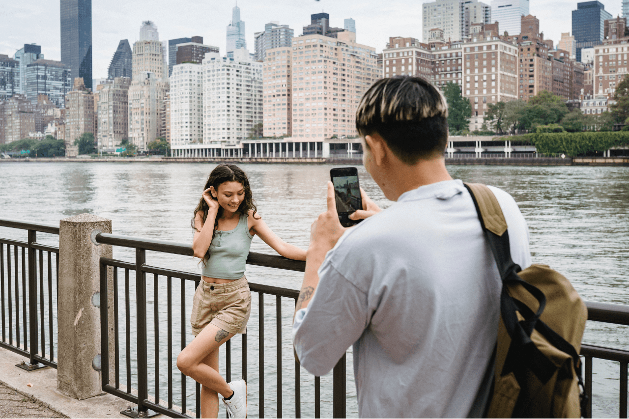 A man takes a picture of his female friend while on vacation in a big city