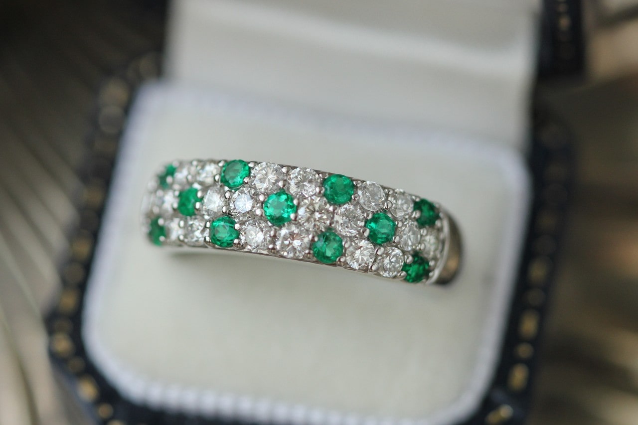 A large white gold wedding band features emeralds and diamonds