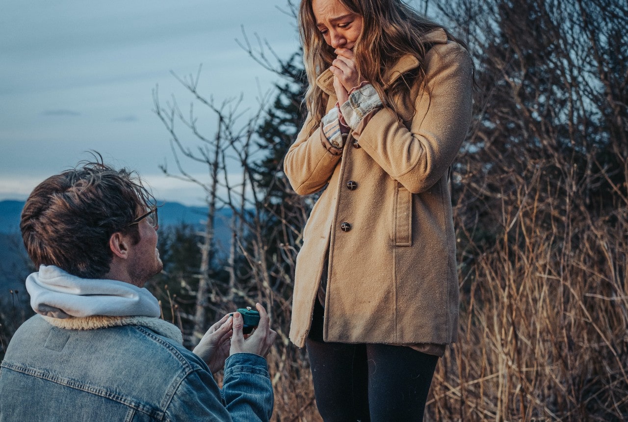 a man on one knee proposing to a woman in the outdoors