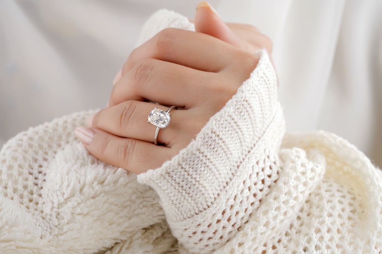 a person’s hands wearing a white sweater and a solitaire engagement ring