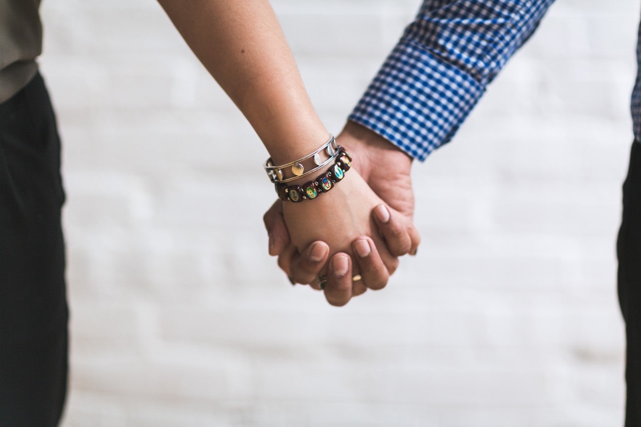 A close-up of a couple holding hands, with emphasis on the two distinctive bracelets stacked on her wrist.