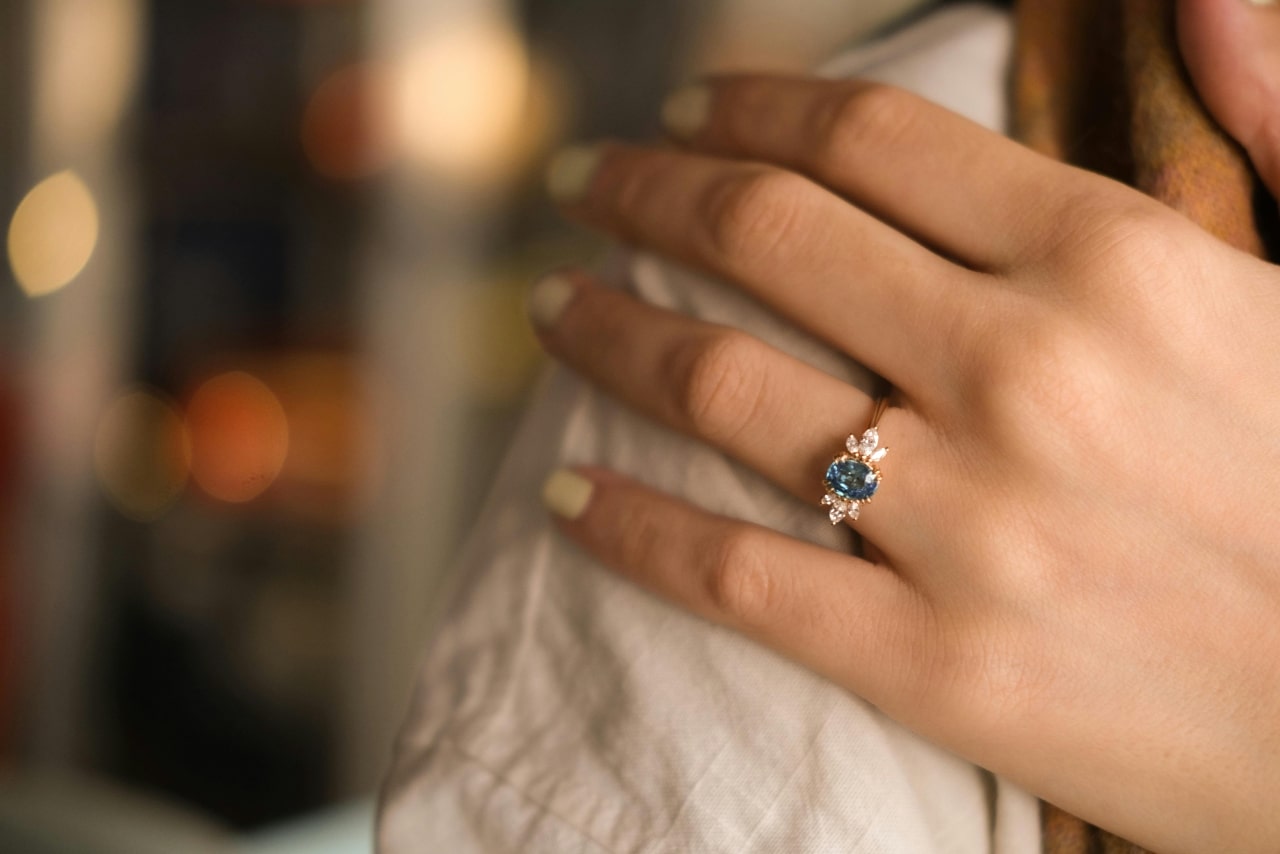 an oval blue topaz center stone with marquise diamonds around it on a yellow gold ring