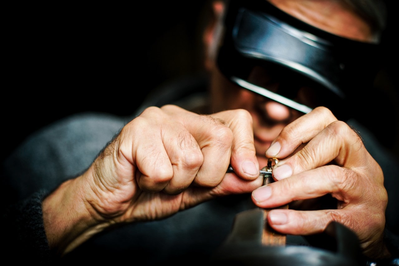 A close-up of a jeweler carefully crafting a ring, using precision tools under a magnifying visor.