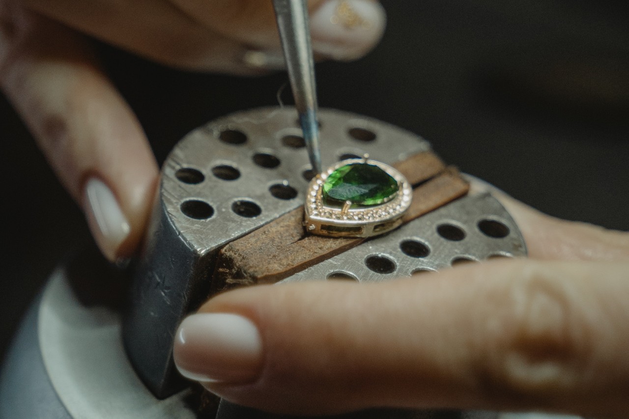 A jewelry expert working on the prongs of a teardrop-shaped emerald stone with a diamond halo.