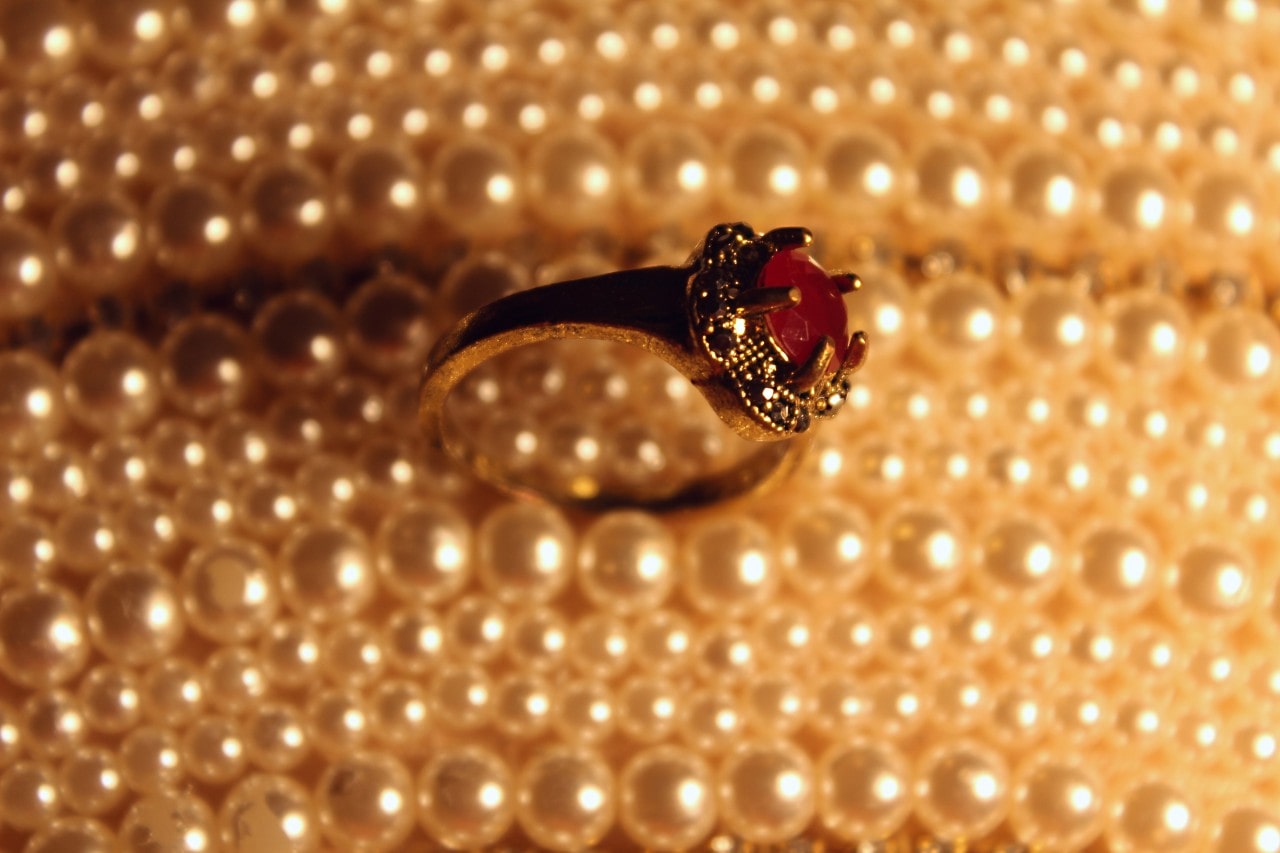 A ruby red and gold fashion ring sitting atop a bunch of strings of pearls.