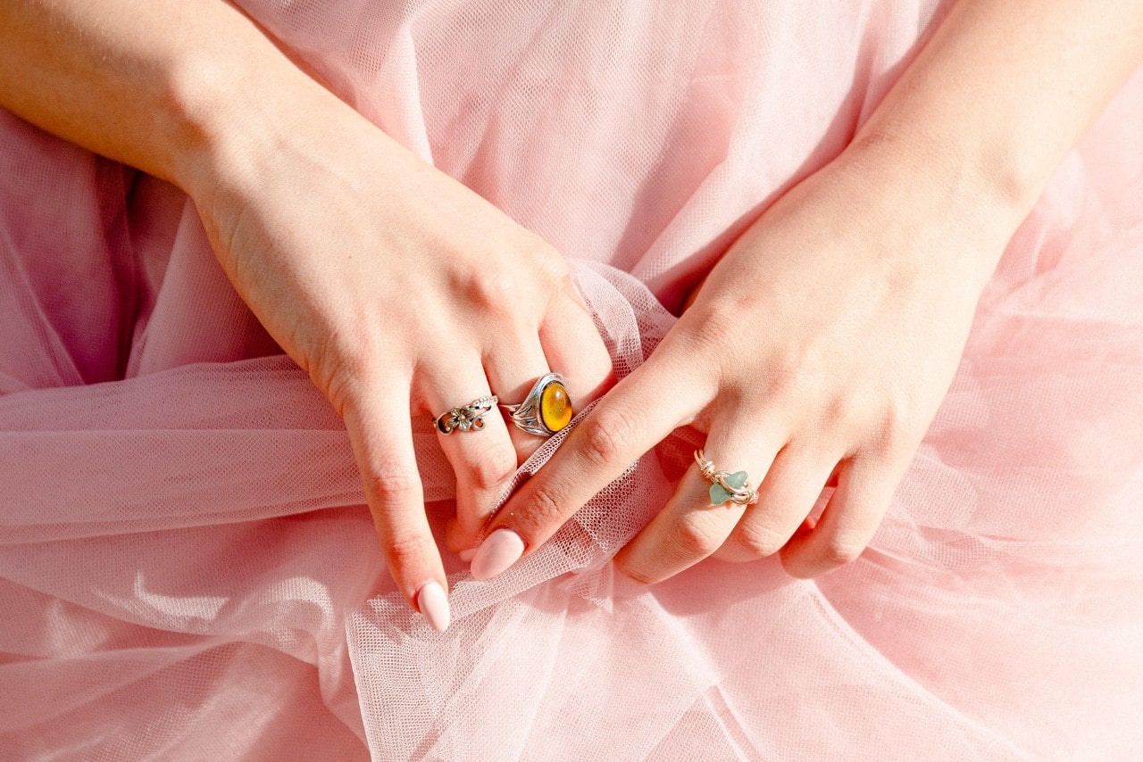 A woman with two gemstone rings and a floral band grabs her pink tulle skirt.