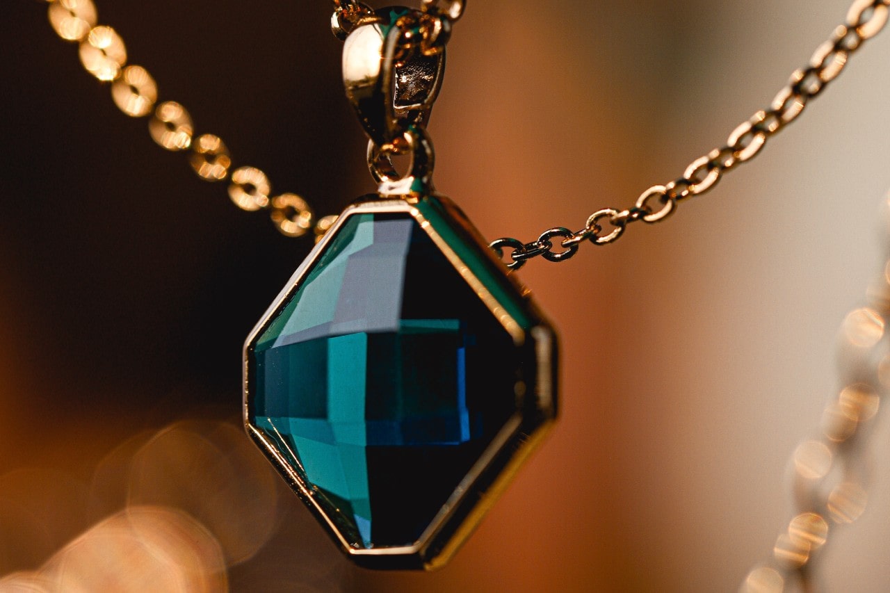 a yellow gold necklace featuring a deep green blue gemstone