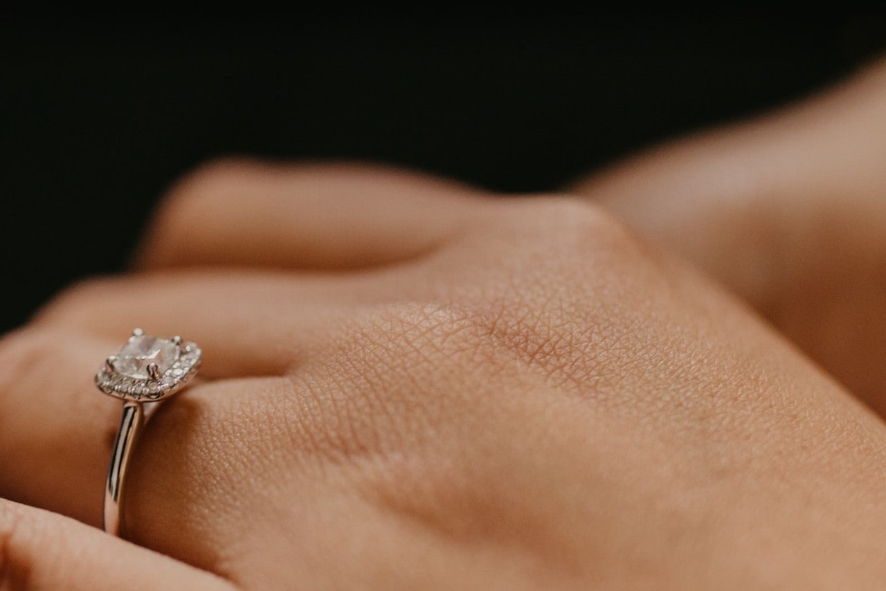 Close-up of a hand wearing a white gold princess-cut engagement ring with halo stones.