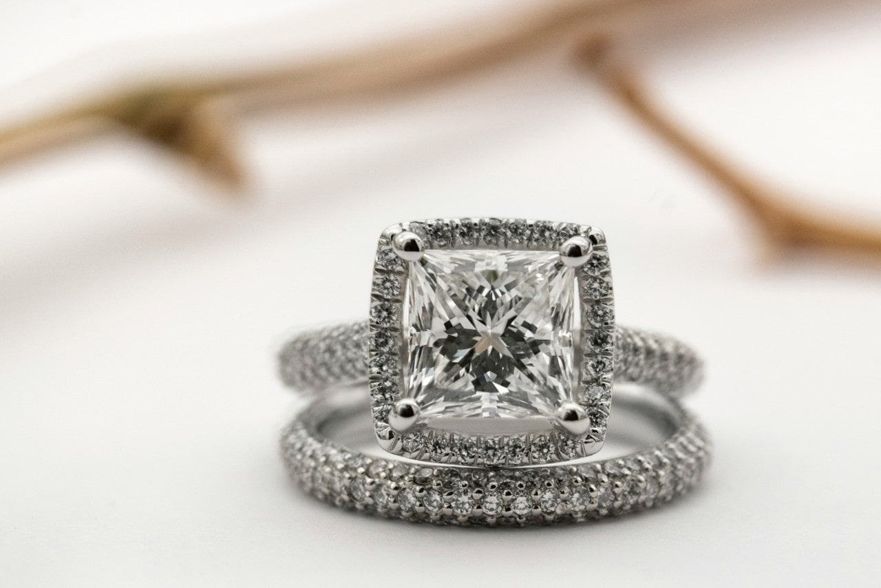 Exquisite princess-cut diamond engagement ring with a halo setting, paired with a matching diamond band, against a soft, blurred background.