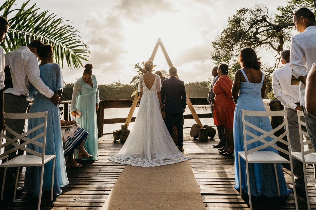 A bride and groom exchange vows at an outdoor altar as the sun sets, bathed in warm golden light, surrounded by family and friends in elegant attire.