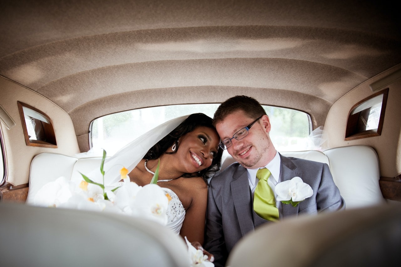 A bride and groom cuddle together in the back of a car after their wedding ceremony.