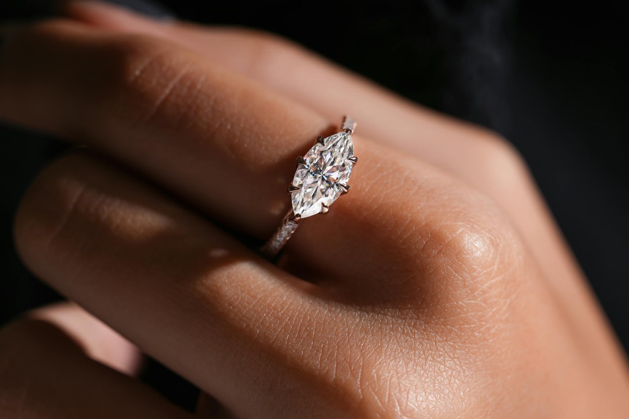 A horizontally set marquise diamond on a side stone ring setting on a woman’s hand.