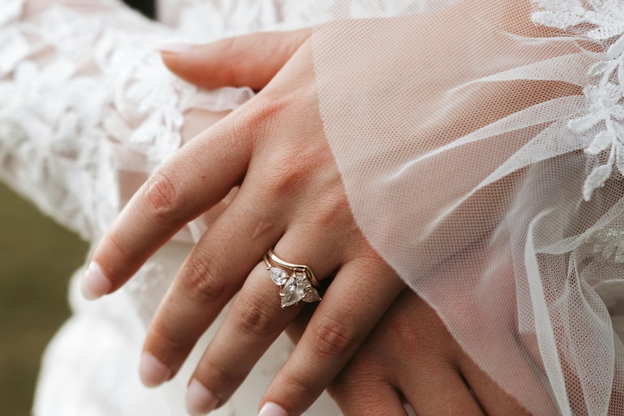 Close-up of a bride's hand with a gold wedding ring, gently resting on lace fabric.