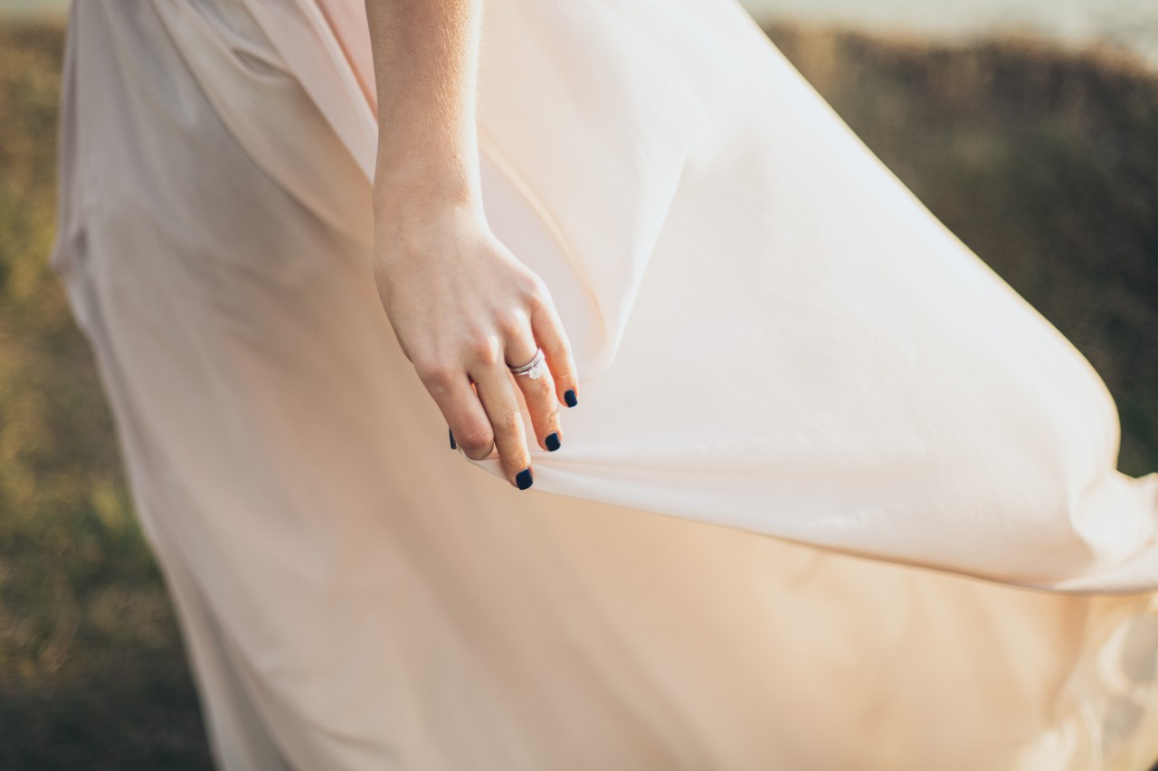 A bride standing in a field with a view on her engagement ring and wedding band A bride standing in a field with a view on her engagement ring and wedding band