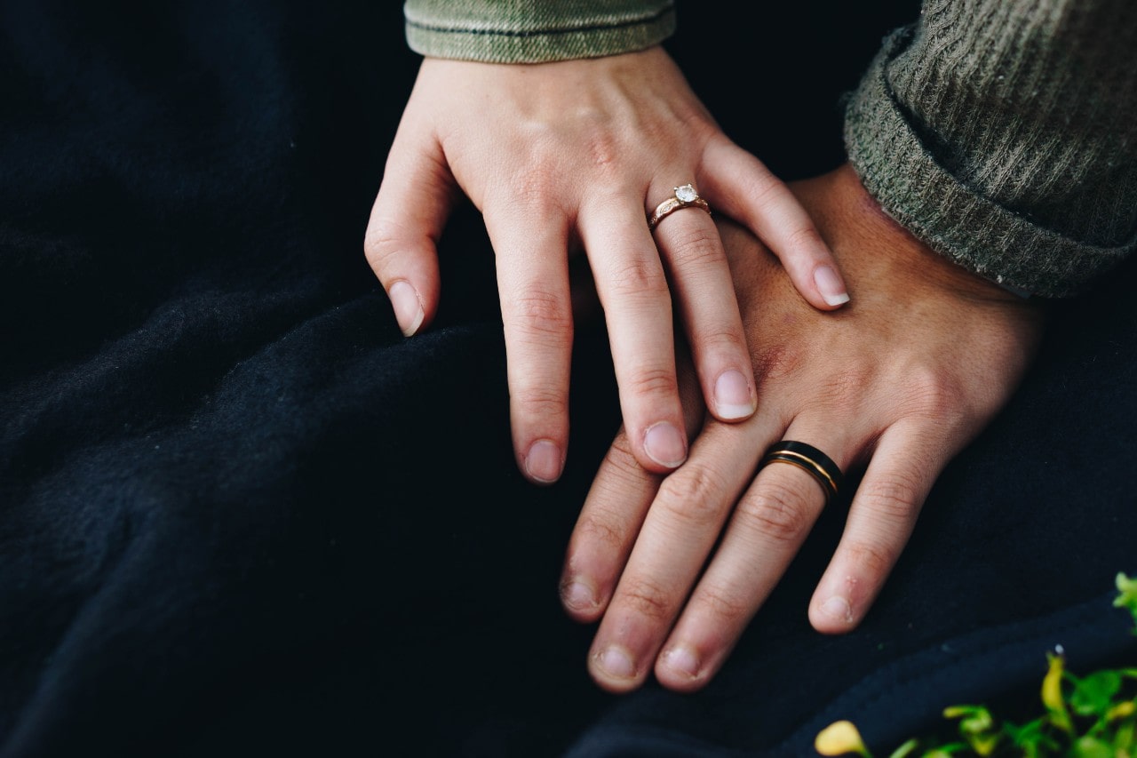 Couple’s hands touching and can see her engagement ring and his wedding band Couple’s hands touching and can see her engagement ring and his wedding band