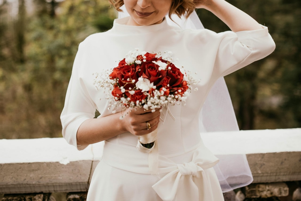 A bride standing outside and see her wedding band and engagement ring holding onto her bouquet of red roses A bride standing outside and see her wedding band and engagement ring holding onto her bouquet of red roses