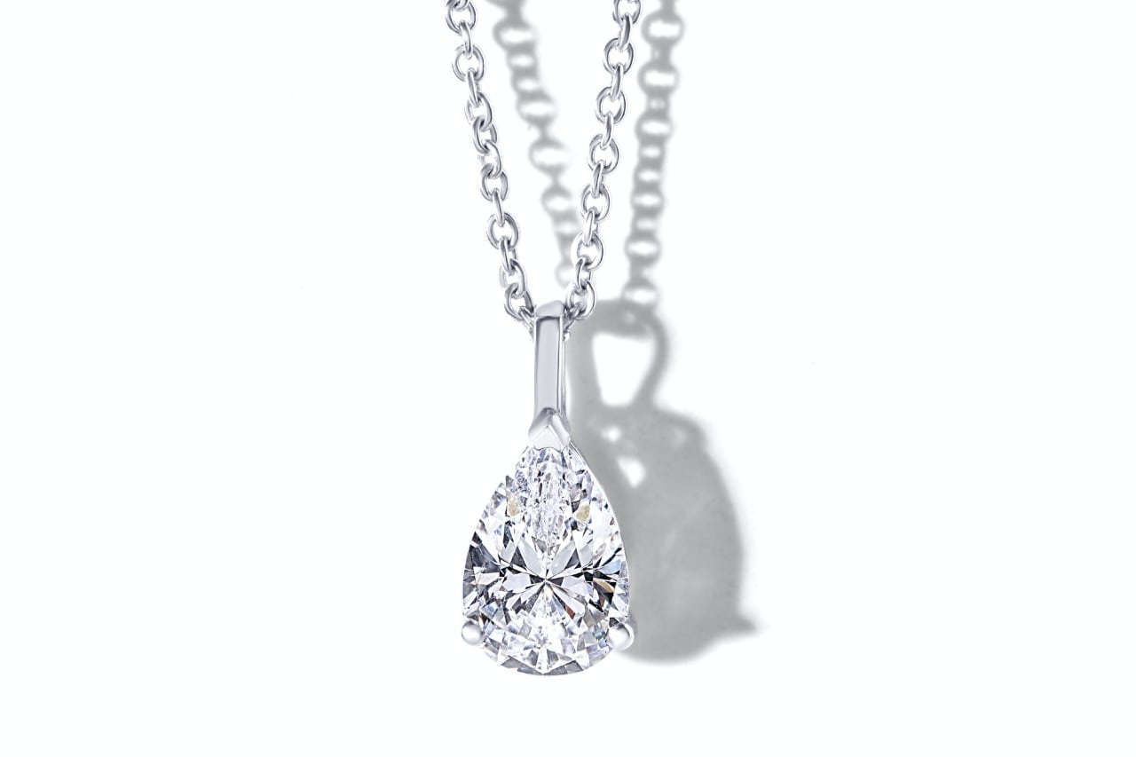A pear-shaped diamond pendant set in white gold hangs from a delicate chain, casting a soft shadow. A pear-shaped diamond pendant set in white gold hangs from a delicate chain, casting a soft shadow.