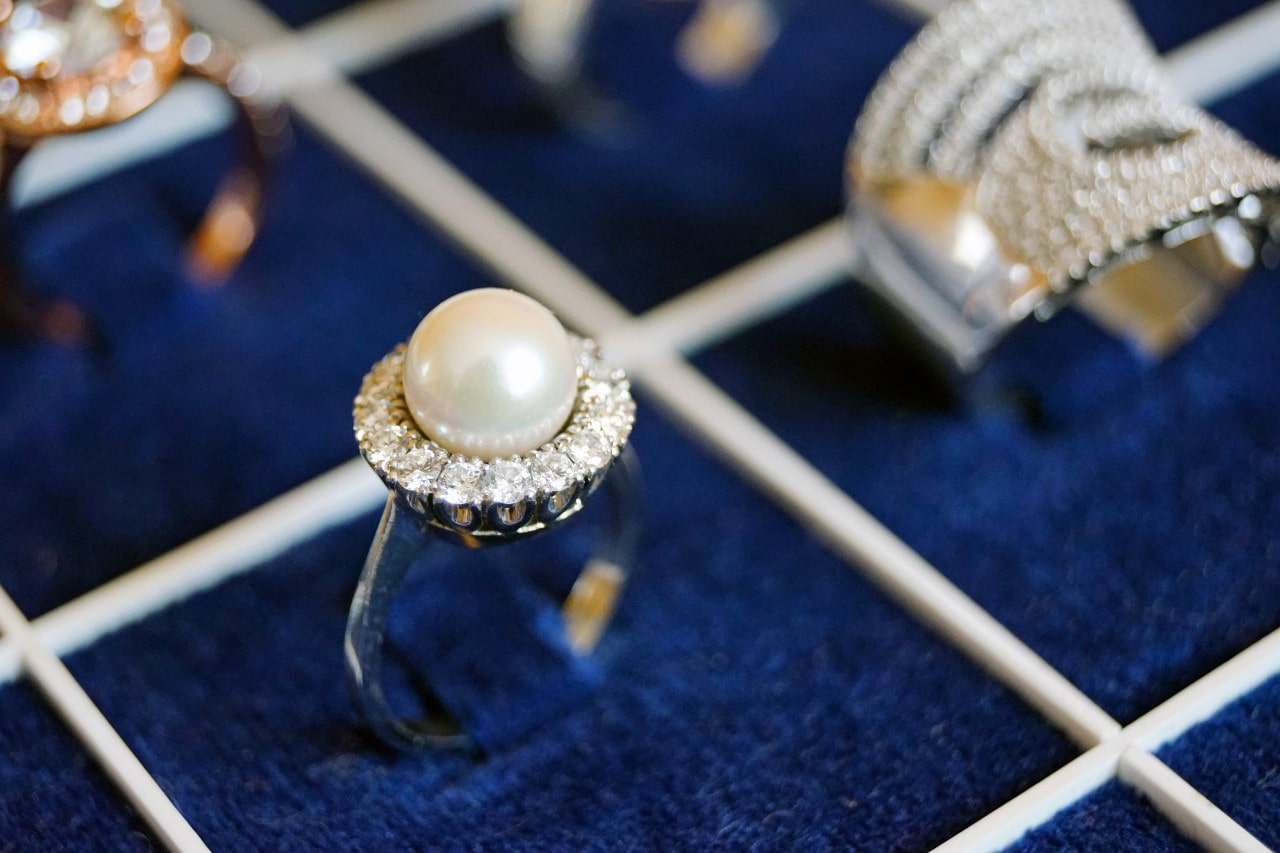 Fashion ring with pearl center stone in a halo setting, surrounded by out-of-focus fashion rings