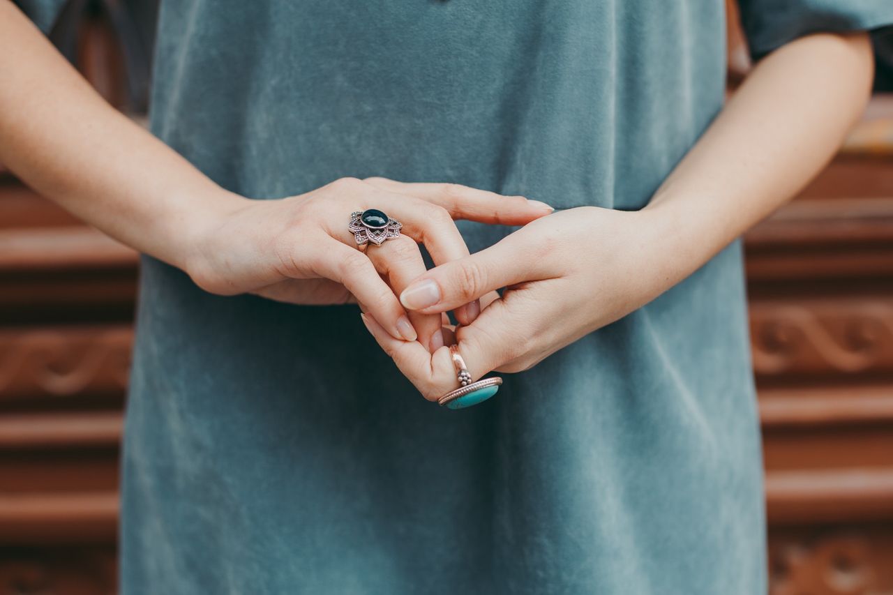 Casually dressed person wears a turquoise and rose gold ring on one hand with an onyx gemstone ring on the other