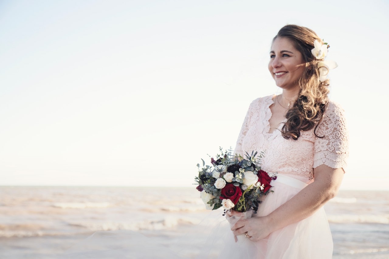 A bride holding a bouquet of red and white roses in a desert.