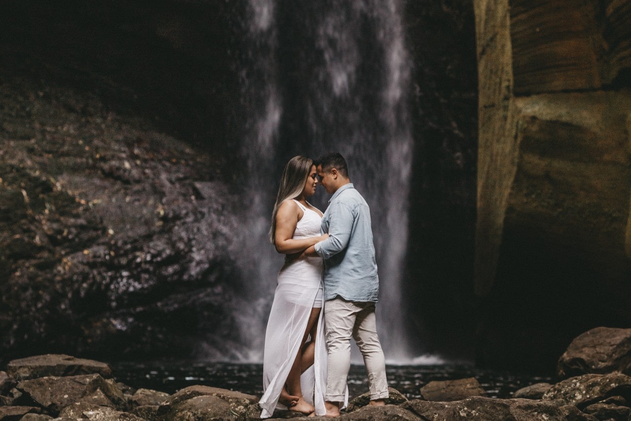 A couple elopes in front of a waterfall, taking a moment to embrace.