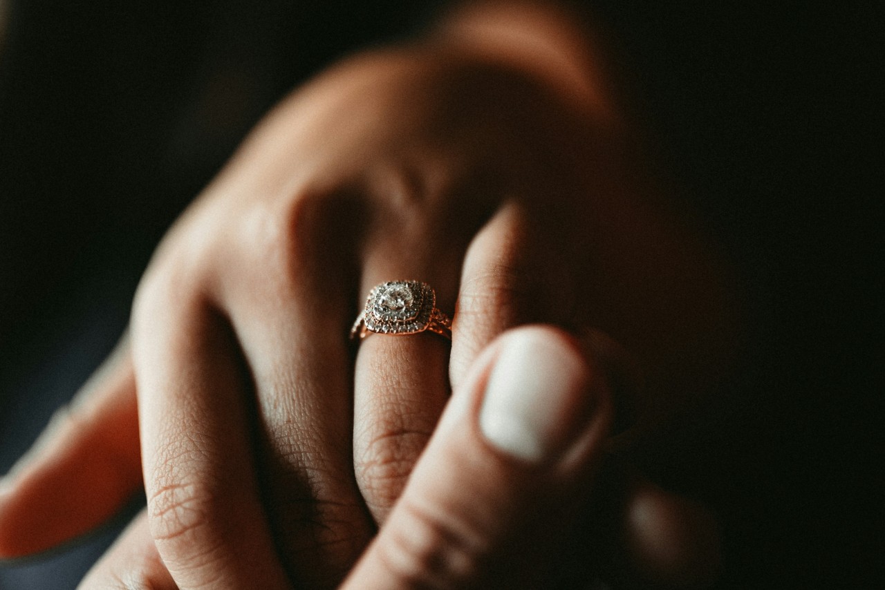 A shot of a woman's hand held by another hand, showcasing a double halo rose gold engagement ring with double row band.