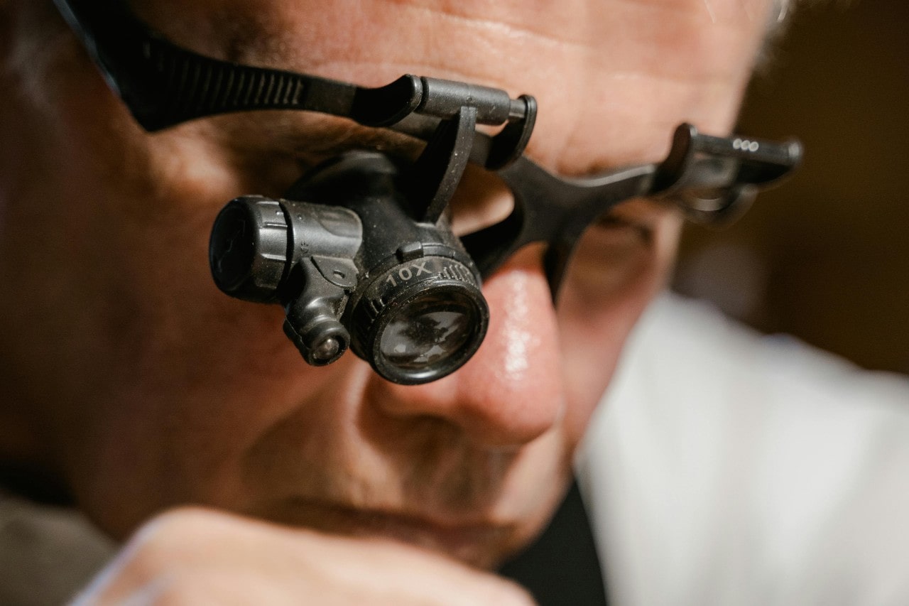 A jeweler inspects a gemstone through a magnifying loupe headset, focusing intently on the details.