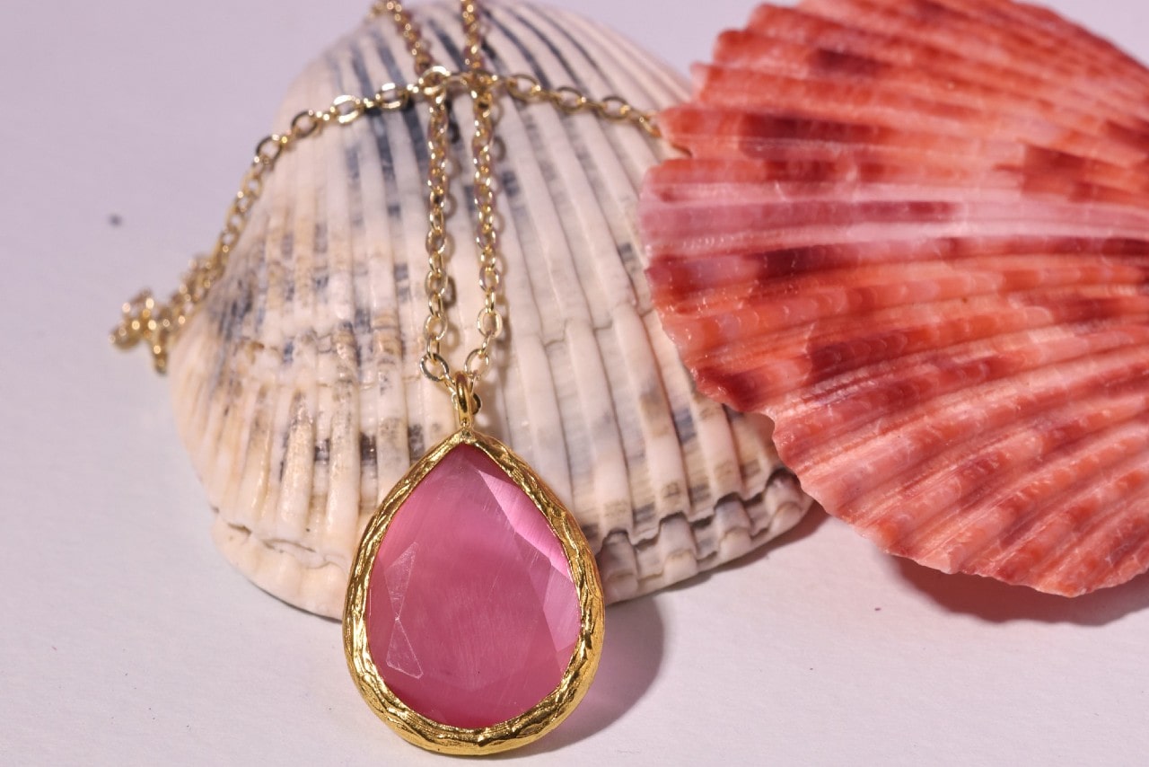 a yellow gold gemstone pendant necklace lying on seashells