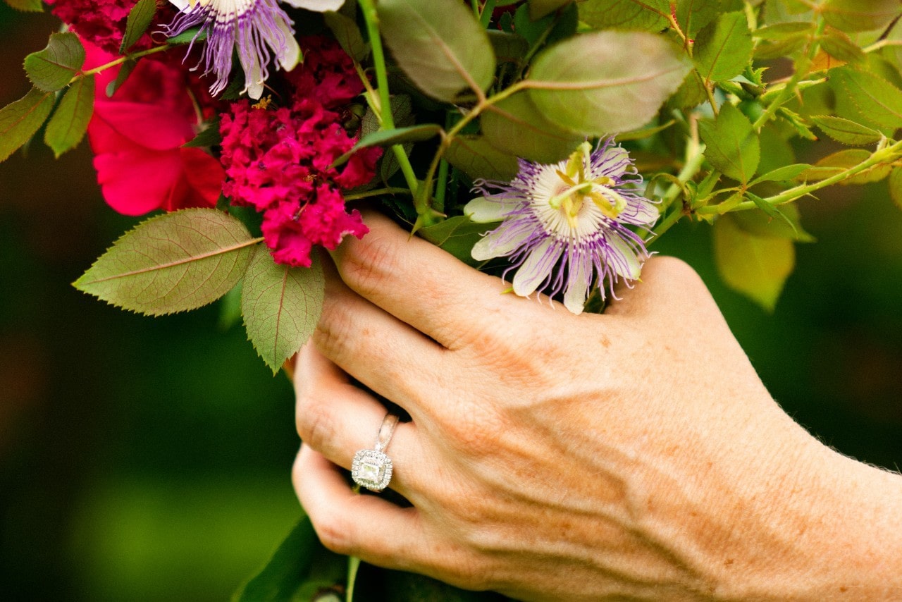 A woman wearing an engagement ring holds a flower bouquet.