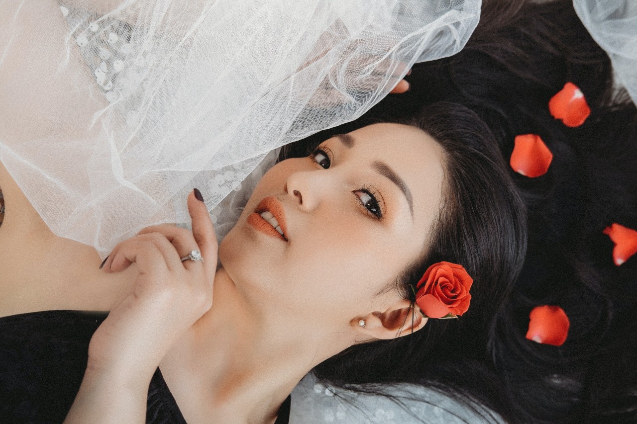 a bride holds her veil while laying down, rose petals in her hair.