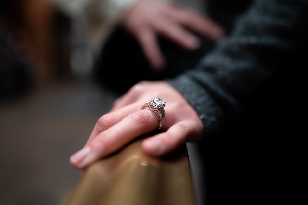 A closeup of a woman’s hand wearing a vintage engagement ring resting on a rail.