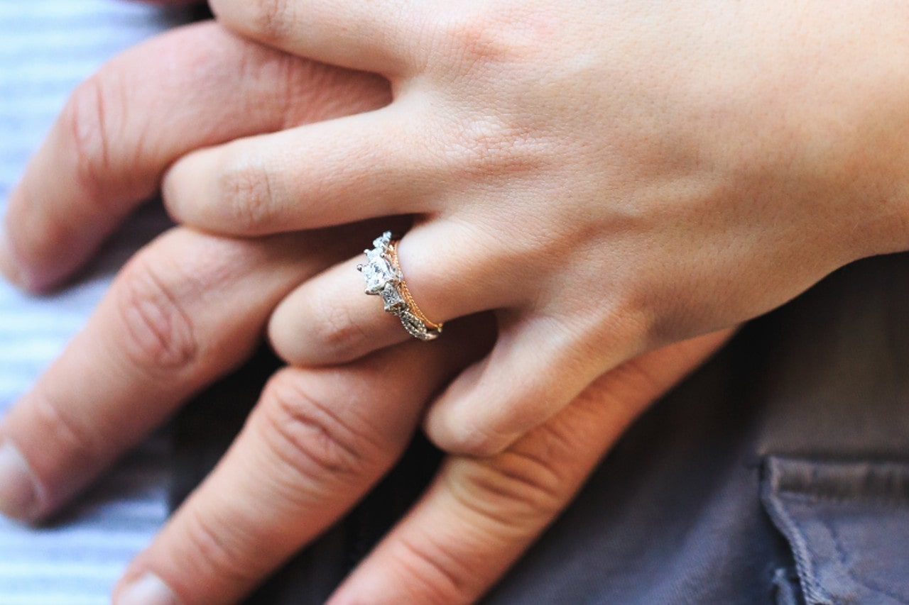 a pair of hands holding, the woman’s hand adorned with a mixed metal, three stone engagement ring