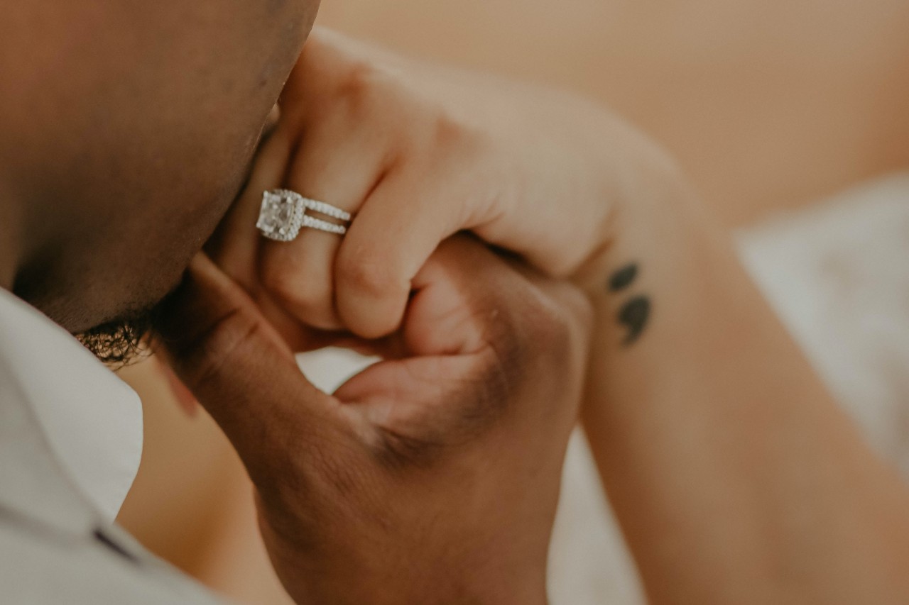 a groom kissing his bride’s hand who is wearing a large, diamond studded engagement ring