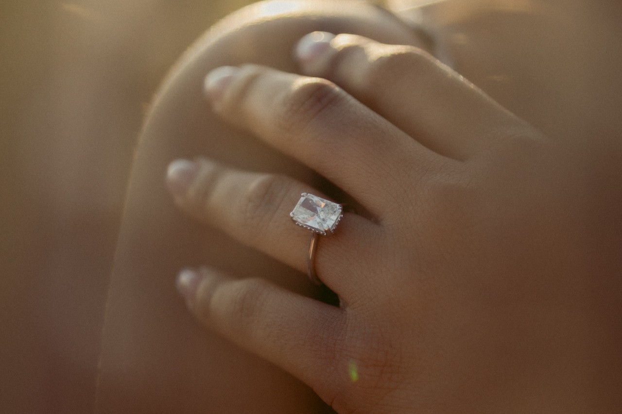 a woman’s hand resting on her shoulder, wearing a large radiant cut engagement ring
