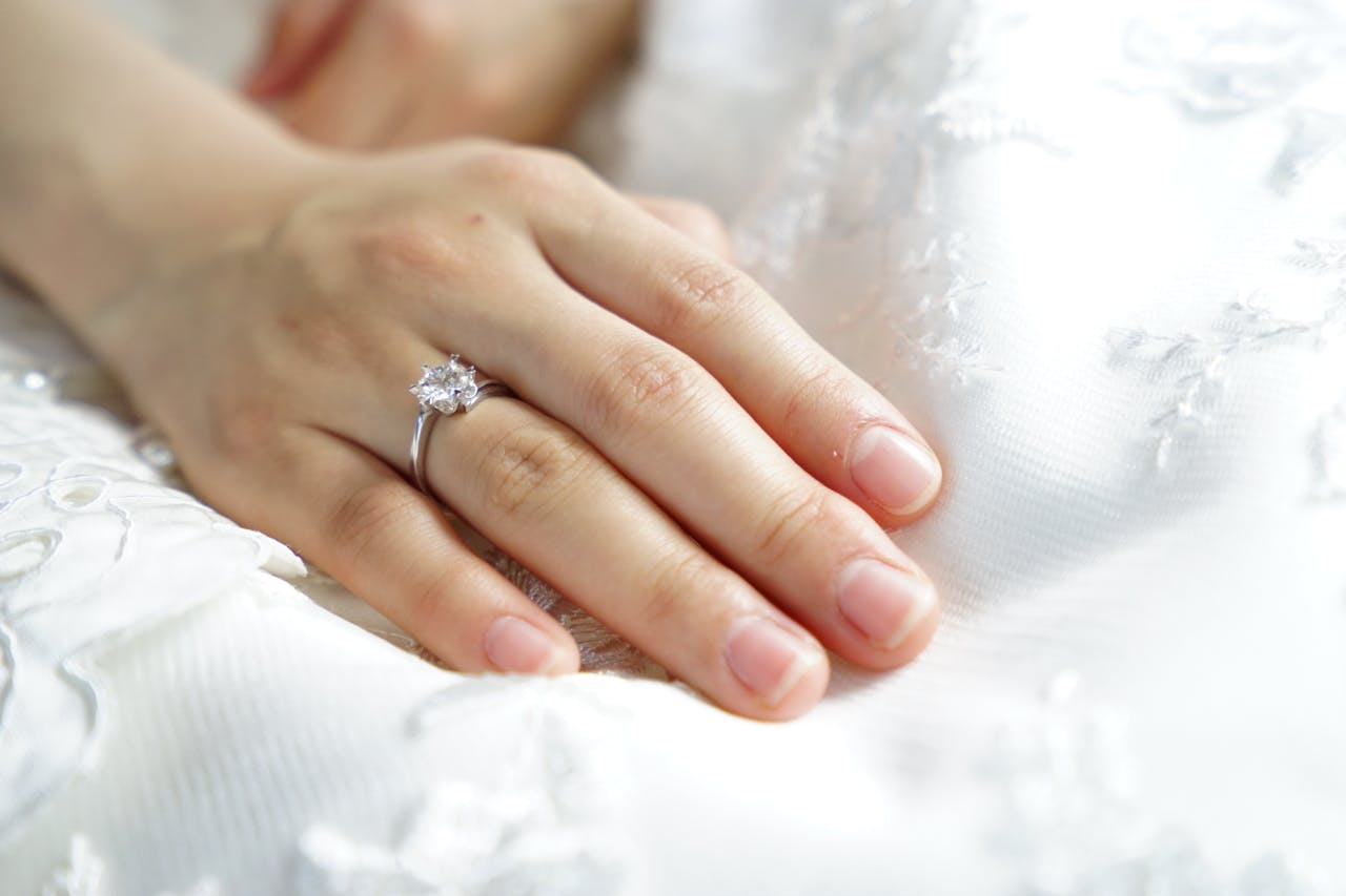 A close up of a woman’s hand on her wedding dress with white gold diamond engagement ring A close up of a woman’s hand on her wedding dress with white gold diamond engagement ring