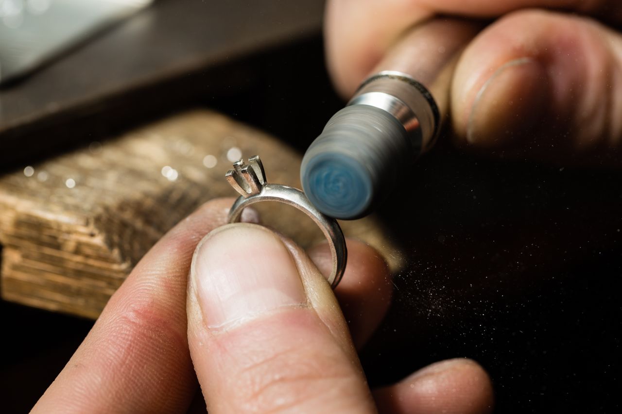 A close up of a jeweler polishing a white gold solitaire engagement ring. A close up of a jeweler polishing a white gold solitaire engagement ring.
