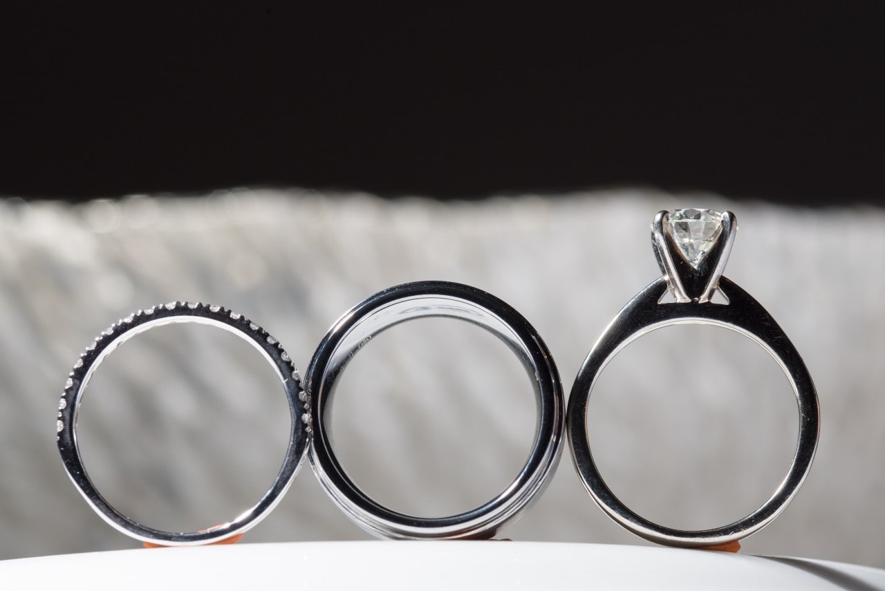 a simple engagement ring sits upright by two wedding bands on a ledge.