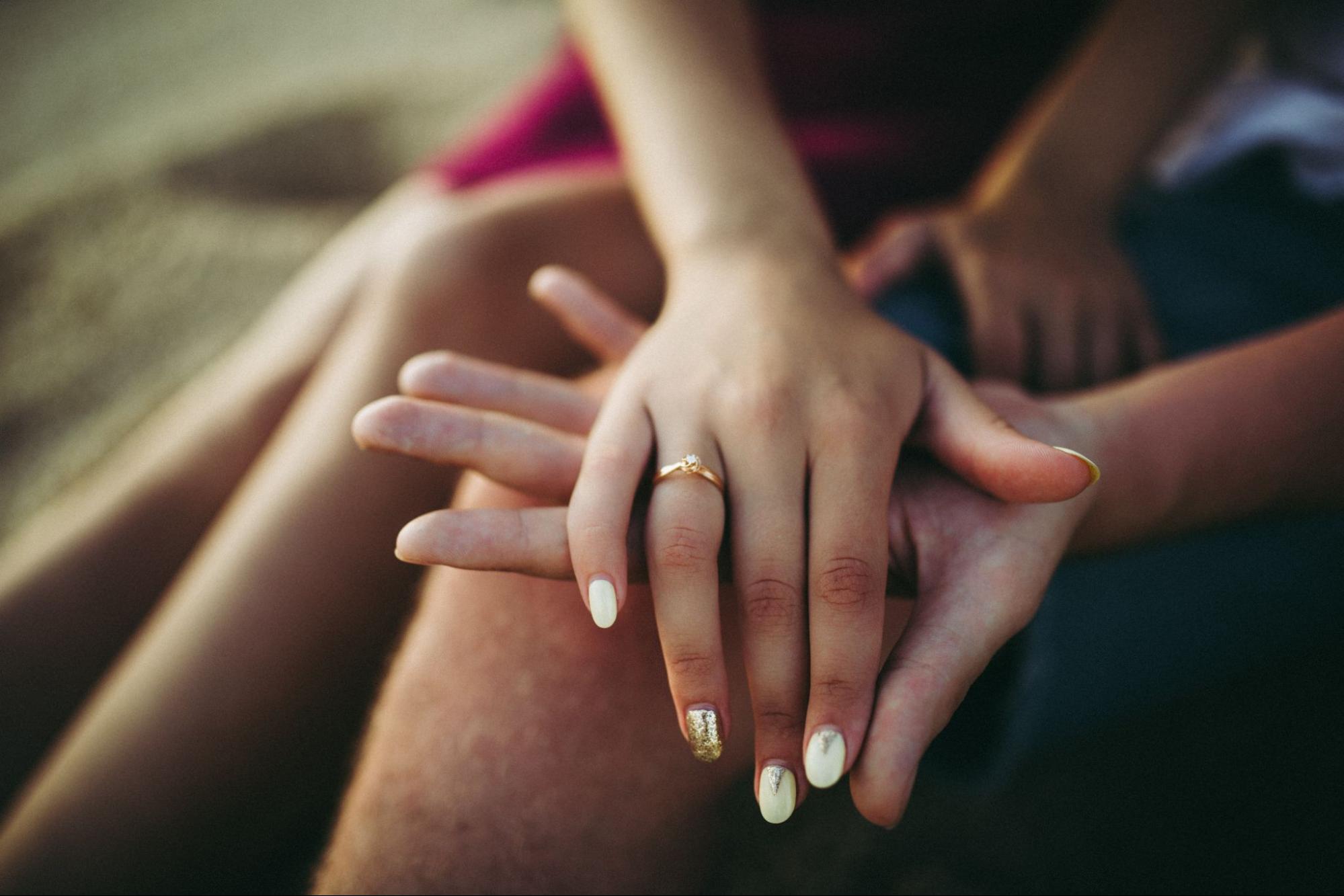 A couple holds hands on the beach, showing off a gold diamond ring.