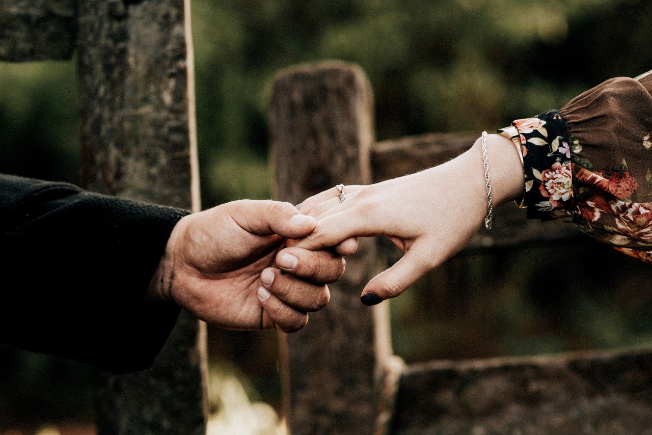 A couple holding hands outside, the woman wearing a simple engagement ring.